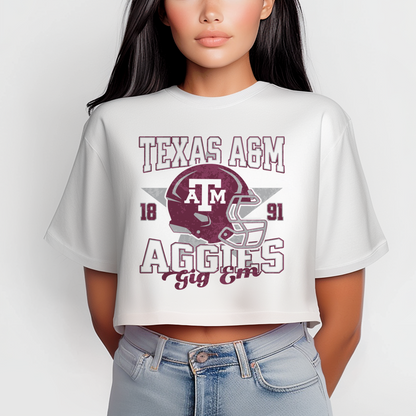 A model wears the White Texas A&M Aggies Football Crop Top. The ﻿Texas A&M Aggies Football﻿ graphic is in bold Multicolor in a Varsity style.