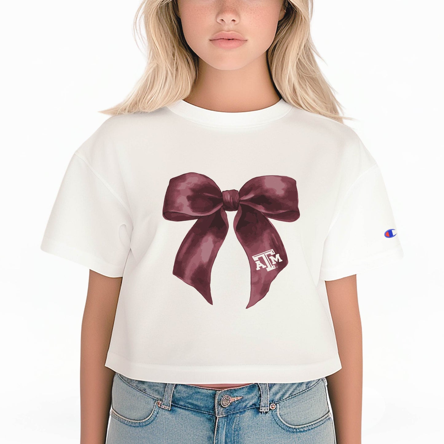 A model wears the White Texas A&M Bow Crop Top.  The ﻿Texas A&M Bow﻿ graphic is in bold Maroon in a coquette style.