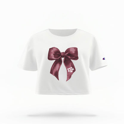 The White Texas A&M Bow Crop Top is shown on a ghost mannequin with a white background. The ﻿Texas A&M Bow﻿ graphic is in bold Maroon in a coquette style.