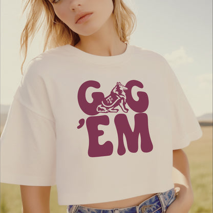 A woman wears the white gig em retro reveille crop top. The shot is up close and she stands in a texas field.