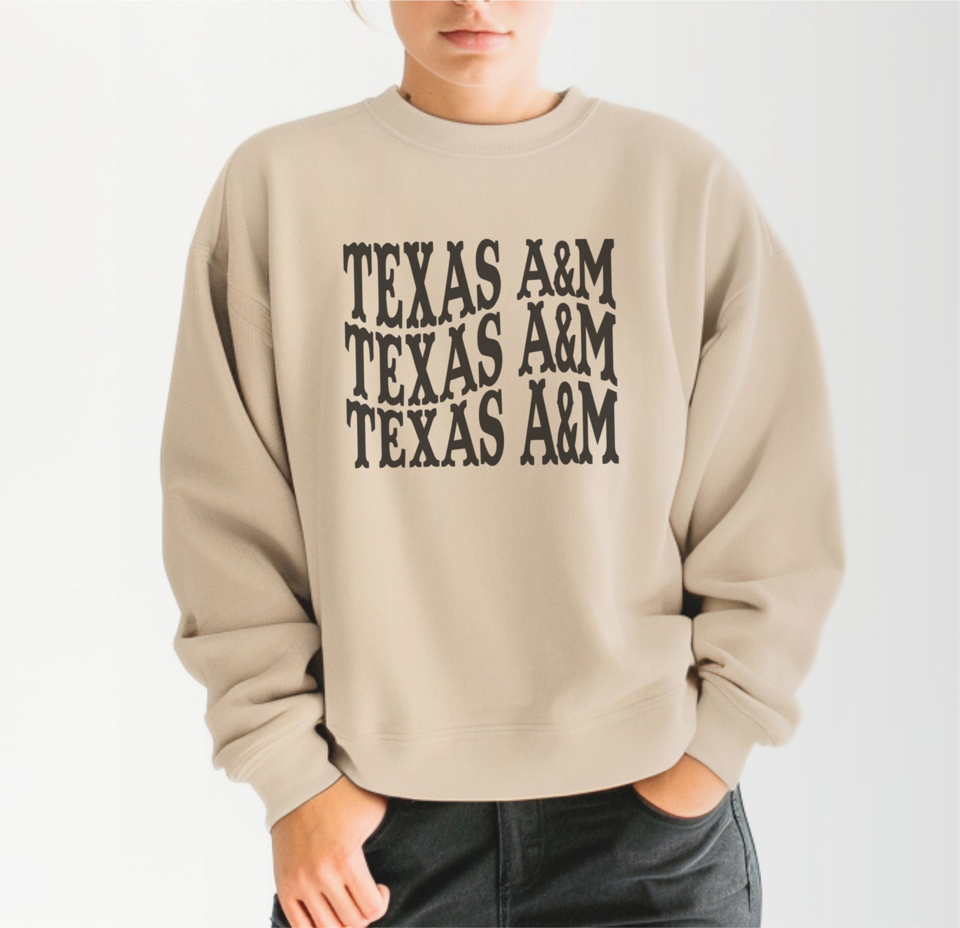 A model wears the Sand Adult Unisex Texas A&M Western Crewneck Sweatshirt.  The ﻿Texas A&M Western﻿ graphic is in bold Black in a Western style.