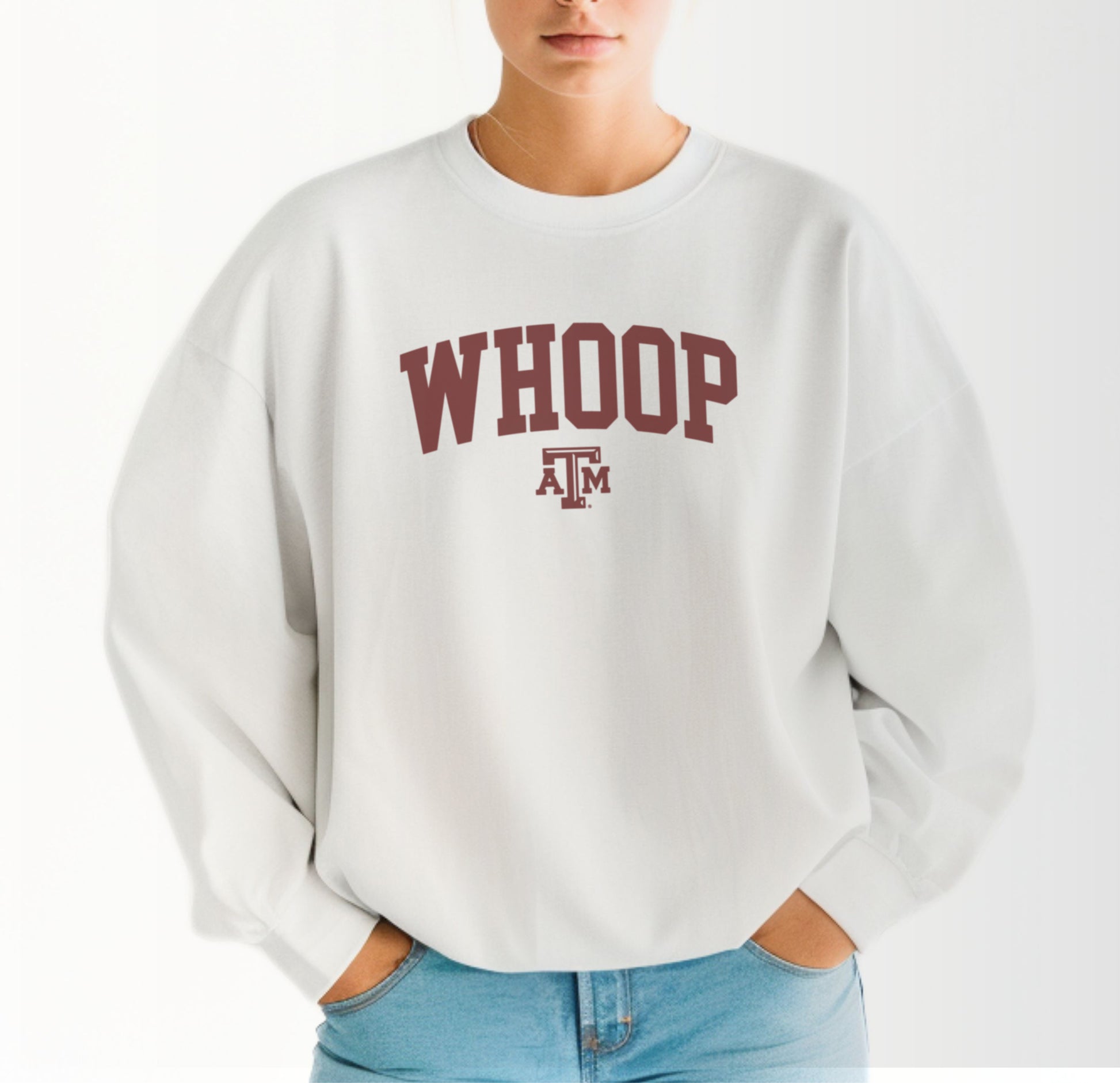 A model wears the White Adult Unisex Texas A&M Whoop Collegiate Crewneck Sweatshirt.  The ﻿Texas A&M Whoop Collegiate﻿ graphic is in bold Maroon in a Varsity style.