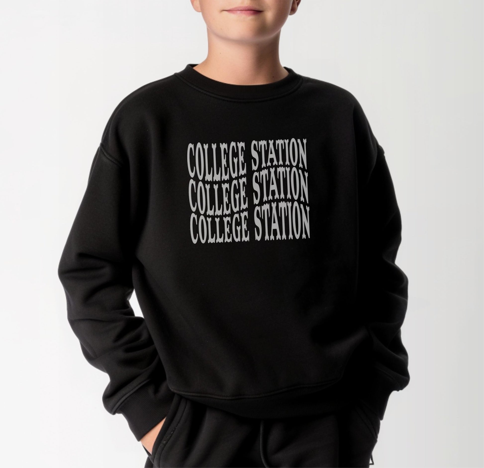 A model wears the Black Youth Unisex College Station Western Crewneck Sweatshirt.  The ﻿College Station Western﻿ graphic is in bold White in a Western style.