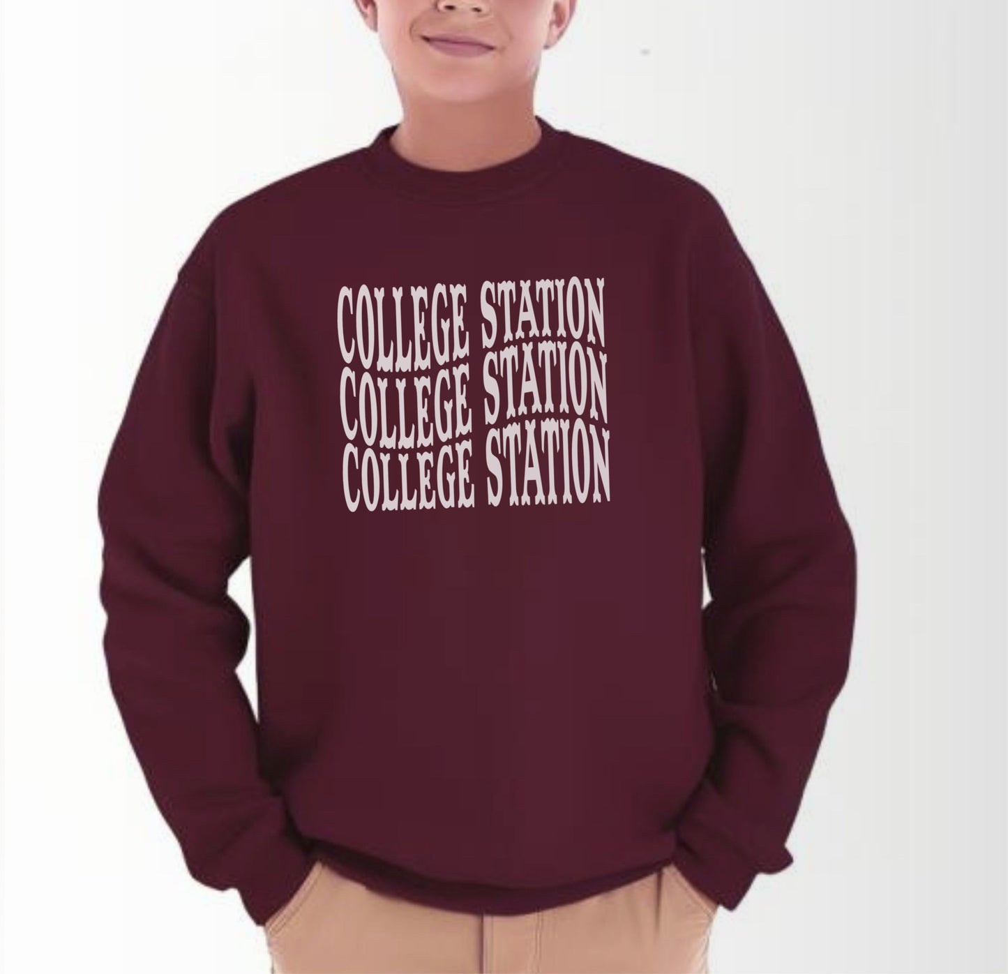 A model wears the Maroon Youth Unisex College Station Western Crewneck Sweatshirt.  The ﻿College Station Western﻿ graphic is in bold White in a Western style.