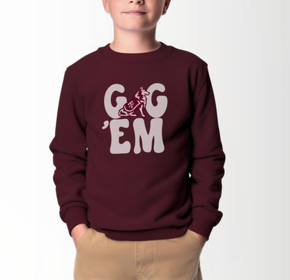 A model wears the Maroon Youth Unisex Texas A&M Gig 'Em Retro Reveille Crewneck Sweatshirt.  The ﻿Texas A&M Gig 'Em Retro Reveille﻿ graphic is in bold White in a Groovy Vintage style.