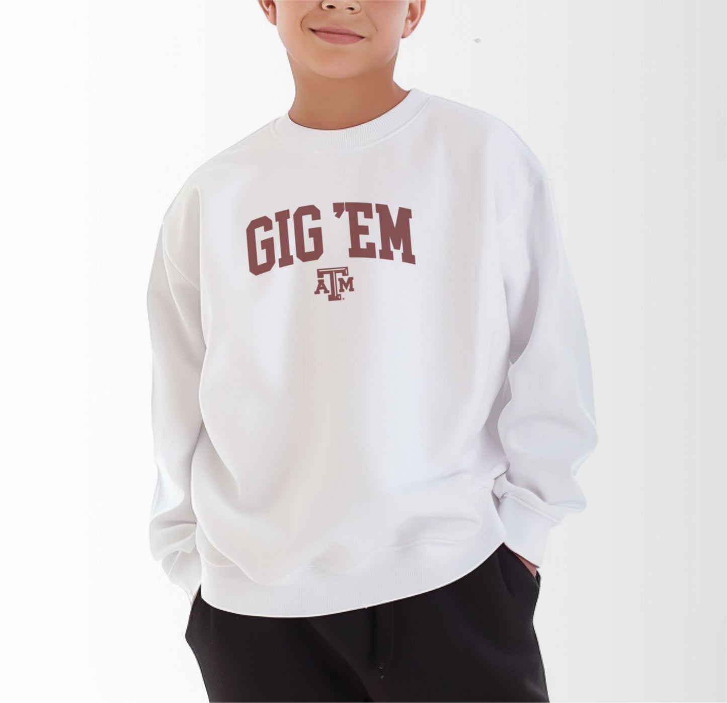 A model wears the White Youth Unisex Texas A&M Gig 'Em Collegiate Crewneck Sweatshirt.  The ﻿Texas A&M Gig 'Em Collegiate﻿ graphic is in bold Maroon in a Collegiate style.