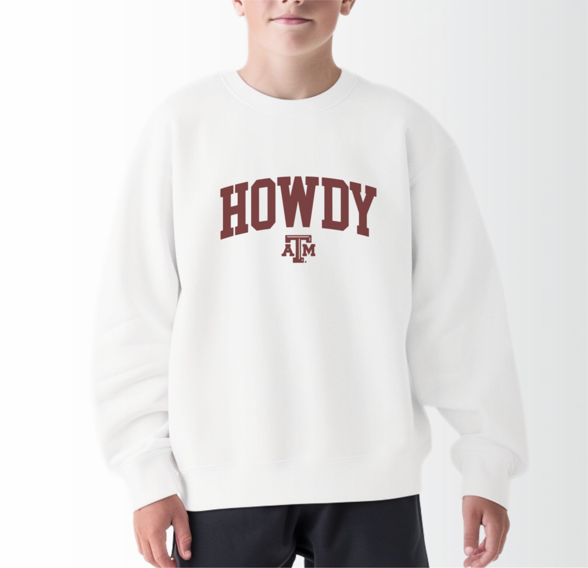 A model wears the White Youth Unisex Texas A&M Howdy Varsity Crewneck Sweatshirt.  The ﻿Texas A&M Howdy Varsity﻿ graphic is in bold Maroon in a Collegiate style.