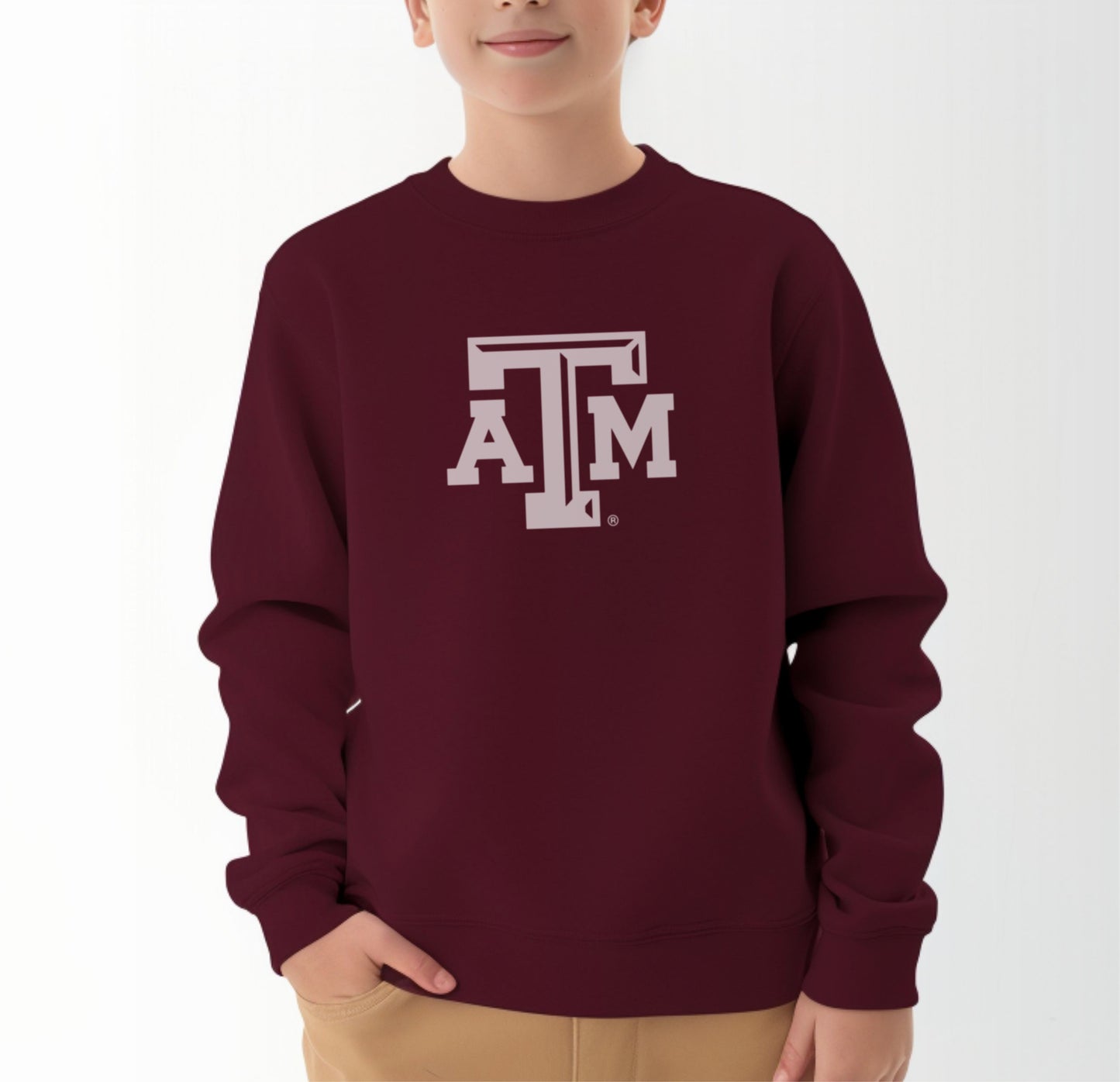 A model wears the Maroon Youth Unisex Texas A&M Logo Crewneck Sweatshirt.  The ﻿Texas A&M Logo﻿ graphic is in bold White in a Varsity style.