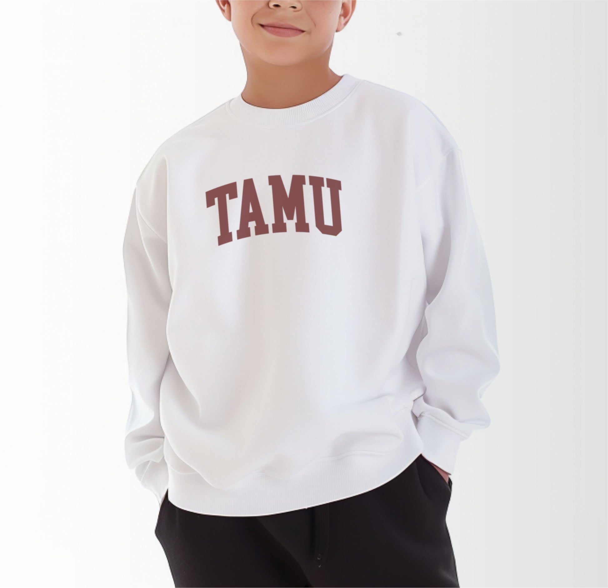 A model wears the White Youth Unisex Texas A&M TAMU Crewneck Sweatshirt.  The ﻿Texas A&M TAMU﻿ graphic is in bold Maroon in a Collegiate style.