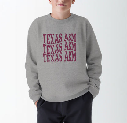 A model wears the Sport Grey Youth Unisex Texas A&M Western Crewneck Sweatshirt.  The ﻿Texas A&M Western﻿ graphic is in bold Maroon in a Western style.