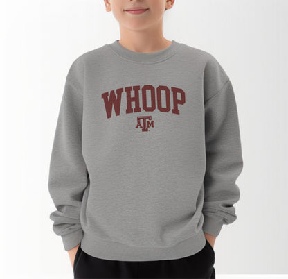 A model wears the Sport Grey Youth Unisex Texas A&M Whoop Collegiate Crewneck Sweatshirt.  The ﻿Texas A&M Whoop Collegiate﻿ graphic is in bold Maroon in a Varsity style.