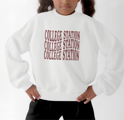 A model wears the White Youth Unisex College Station Western Crewneck Sweatshirt.  The ﻿College Station Western﻿ graphic is in bold Maroon in a Western style.