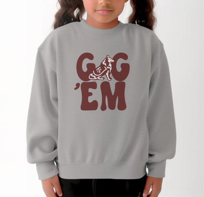 A model wears the Sport Grey Youth Unisex Texas A&M Gig 'Em Retro Reveille Crewneck Sweatshirt.  The ﻿Texas A&M Gig 'Em Retro Reveille﻿ graphic is in bold Maroon in a Groovy Vintage style.