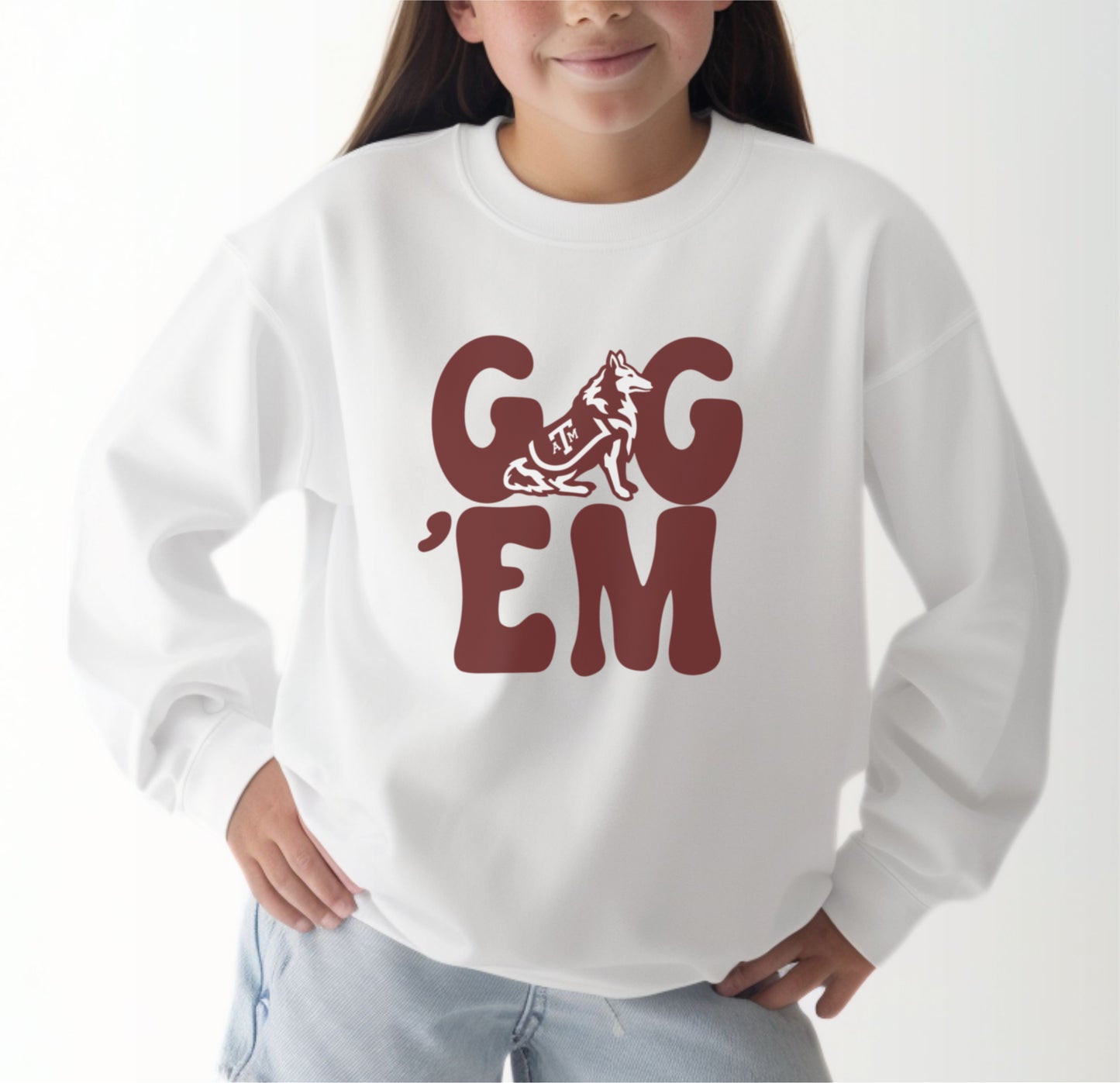 A model wears the White Youth Unisex Texas A&M Gig 'Em Retro Reveille Crewneck Sweatshirt.  The ﻿Texas A&M Gig 'Em Retro Reveille﻿ graphic is in bold Maroon in a Groovy Vintage style.