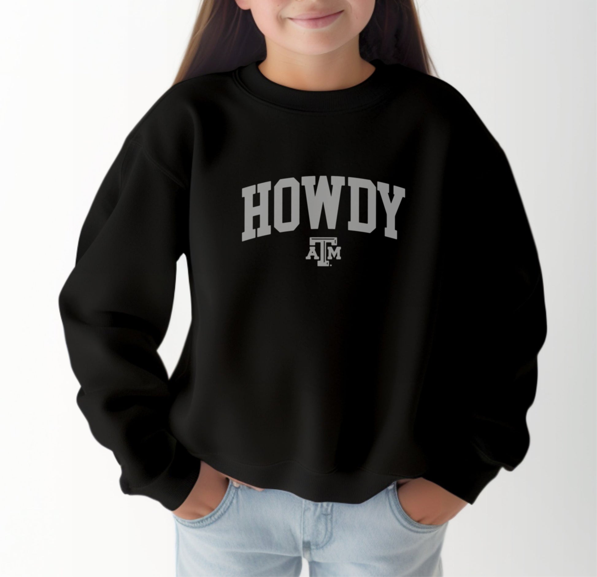 A model wears the Black Youth Unisex Texas A&M Howdy Varsity Crewneck Sweatshirt.  The ﻿Texas A&M Howdy Varsity﻿ graphic is in bold White in a Collegiate style.