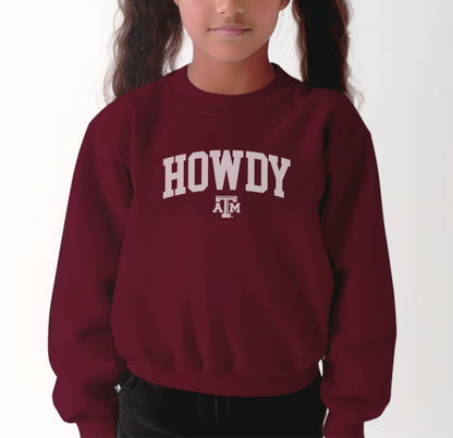 A model wears the Maroon Youth Unisex Texas A&M Howdy Varsity Crewneck Sweatshirt.  The ﻿Texas A&M Howdy Varsity﻿ graphic is in bold White in a Collegiate style.