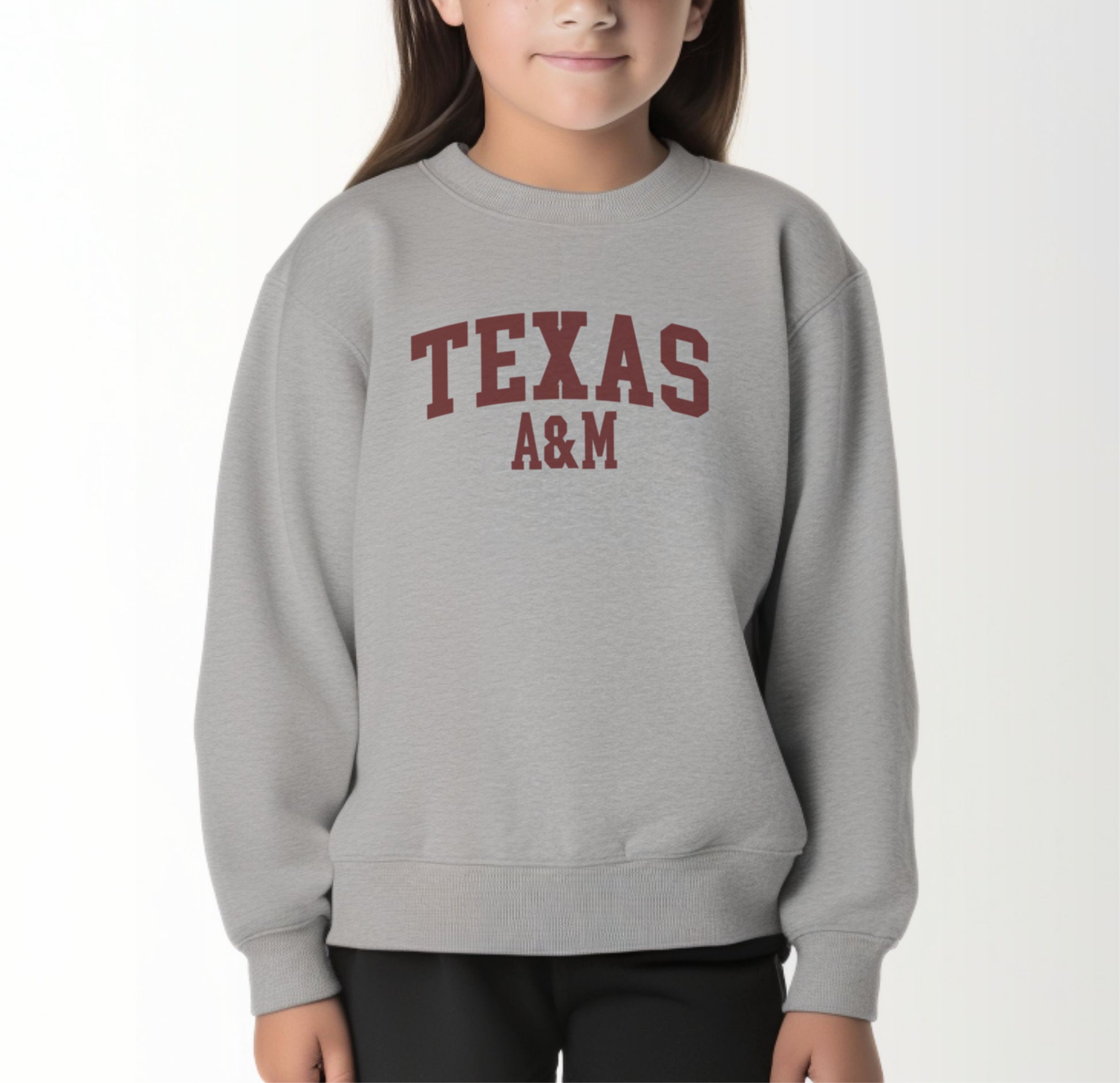 A model wears the Sport Grey Youth Unisex Texas A&M Varsity Crewneck Sweatshirt.  The ﻿Texas A&M Varsity﻿ graphic is in bold Maroon in a Collegiate style.