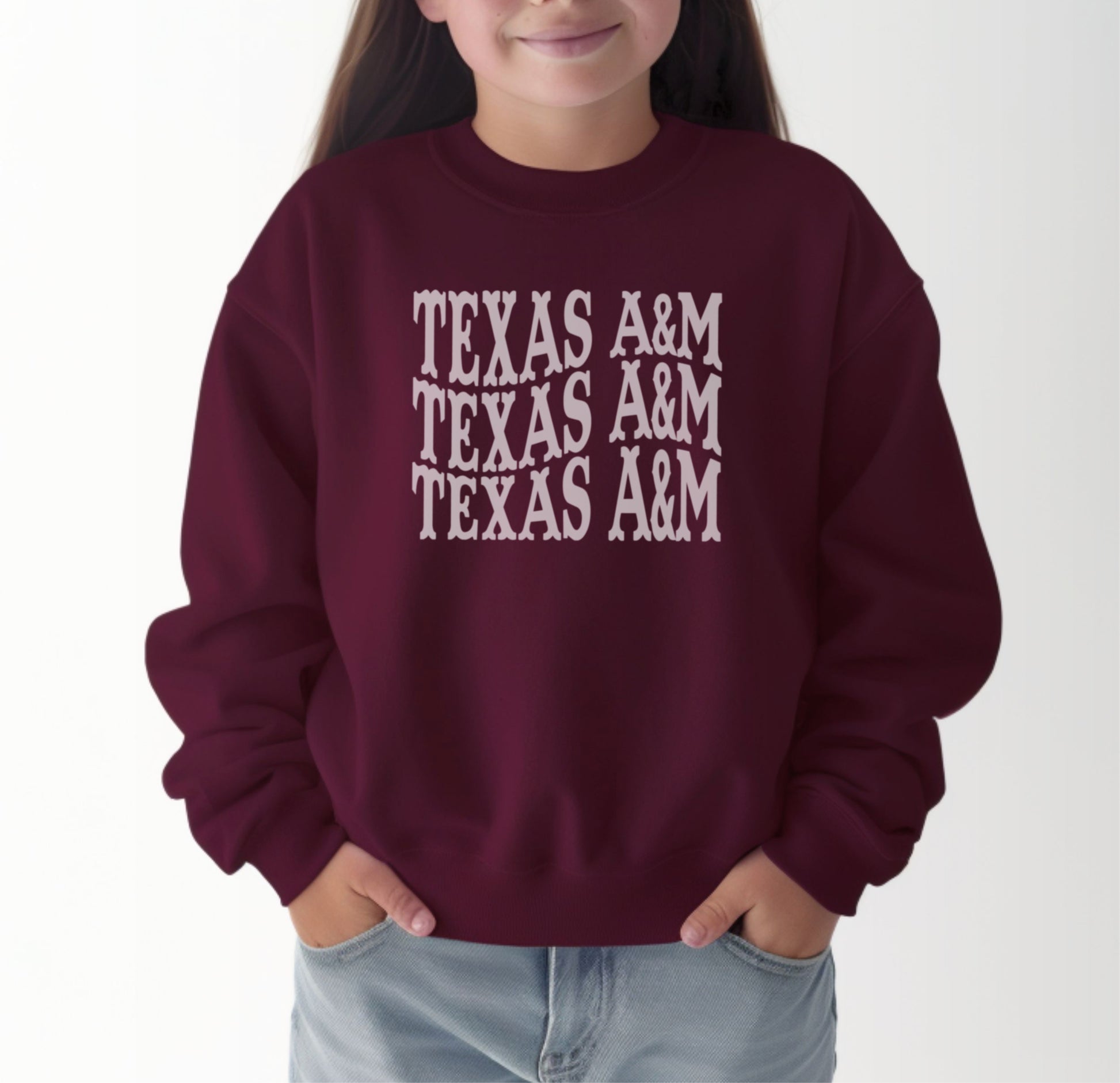 A model wears the Maroon Youth Unisex Texas A&M Western Crewneck Sweatshirt.  The ﻿Texas A&M Western﻿ graphic is in bold White in a Western style.