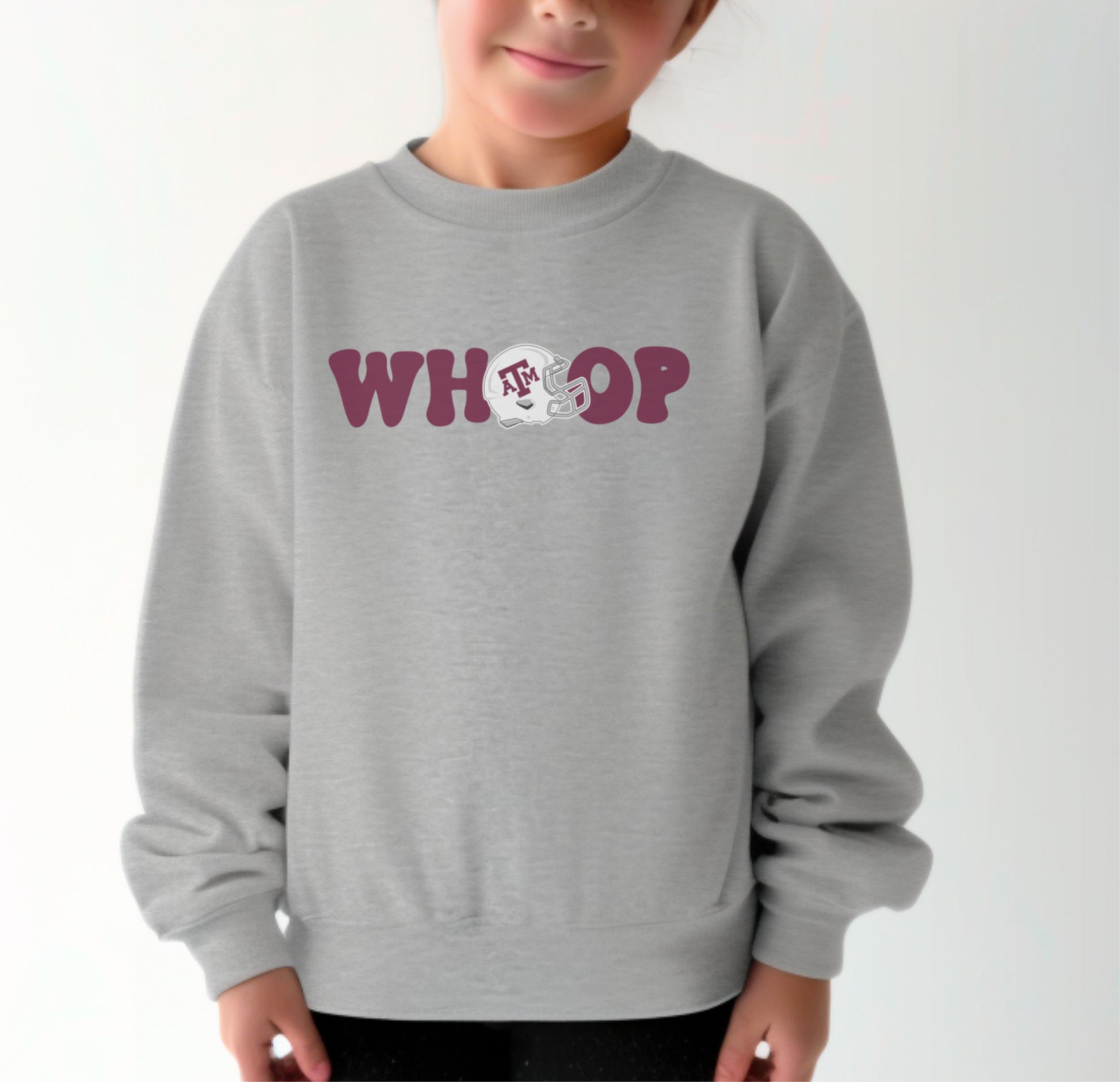 A model wears the Sport Grey Youth Unisex Texas A&M Retro Whoop Crewneck Sweatshirt.  The ﻿Texas A&M Retro Whoop﻿ graphic is in bold Maroon in a Vintage style.