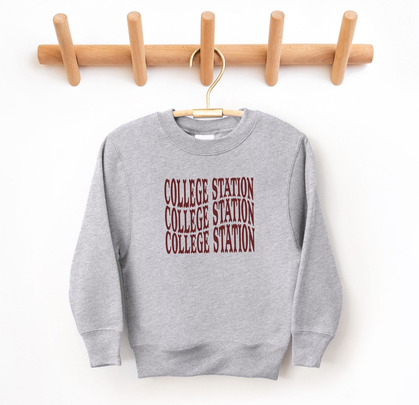 The Sport Grey Youth Unisex College Station Western Crewneck Sweatshirt lays flat on a white background. The ﻿College Station Western﻿ graphic is in bold Maroon in a Western style.