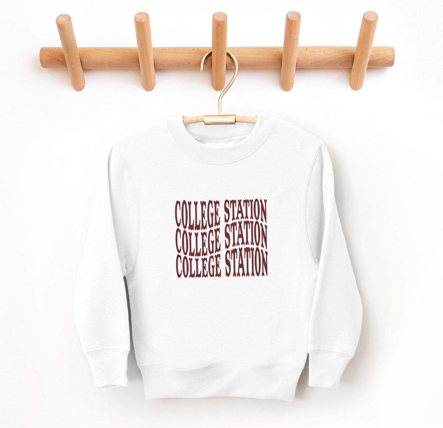 The White Youth Unisex College Station Western Crewneck Sweatshirt lays flat on a white background. The ﻿College Station Western﻿ graphic is in bold Maroon in a Western style.