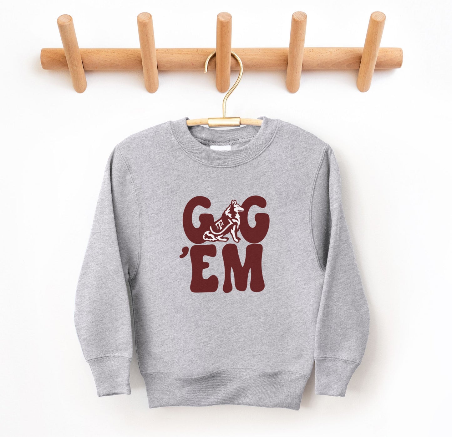 The Sport Grey Youth Unisex Texas A&M Gig 'Em Retro Reveille Crewneck Sweatshirt lays flat on a white background. The ﻿Texas A&M Gig 'Em Retro Reveille﻿ graphic is in bold Maroon in a Groovy Vintage style.