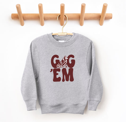 The Sport Grey Youth Unisex Texas A&M Gig 'Em Retro Reveille Crewneck Sweatshirt lays flat on a white background. The ﻿Texas A&M Gig 'Em Retro Reveille﻿ graphic is in bold Maroon in a Groovy Vintage style.