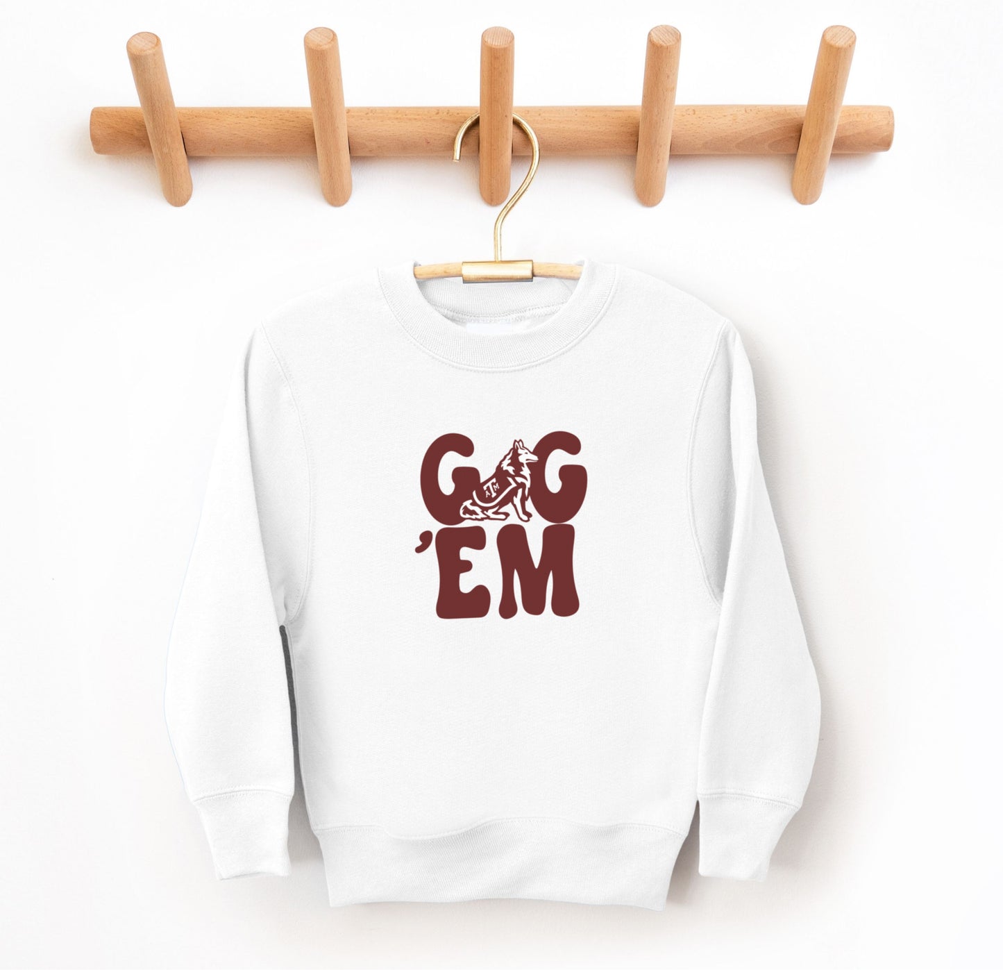 The White Youth Unisex Texas A&M Gig 'Em Retro Reveille Crewneck Sweatshirt lays flat on a white background. The ﻿Texas A&M Gig 'Em Retro Reveille﻿ graphic is in bold Maroon in a Groovy Vintage style.