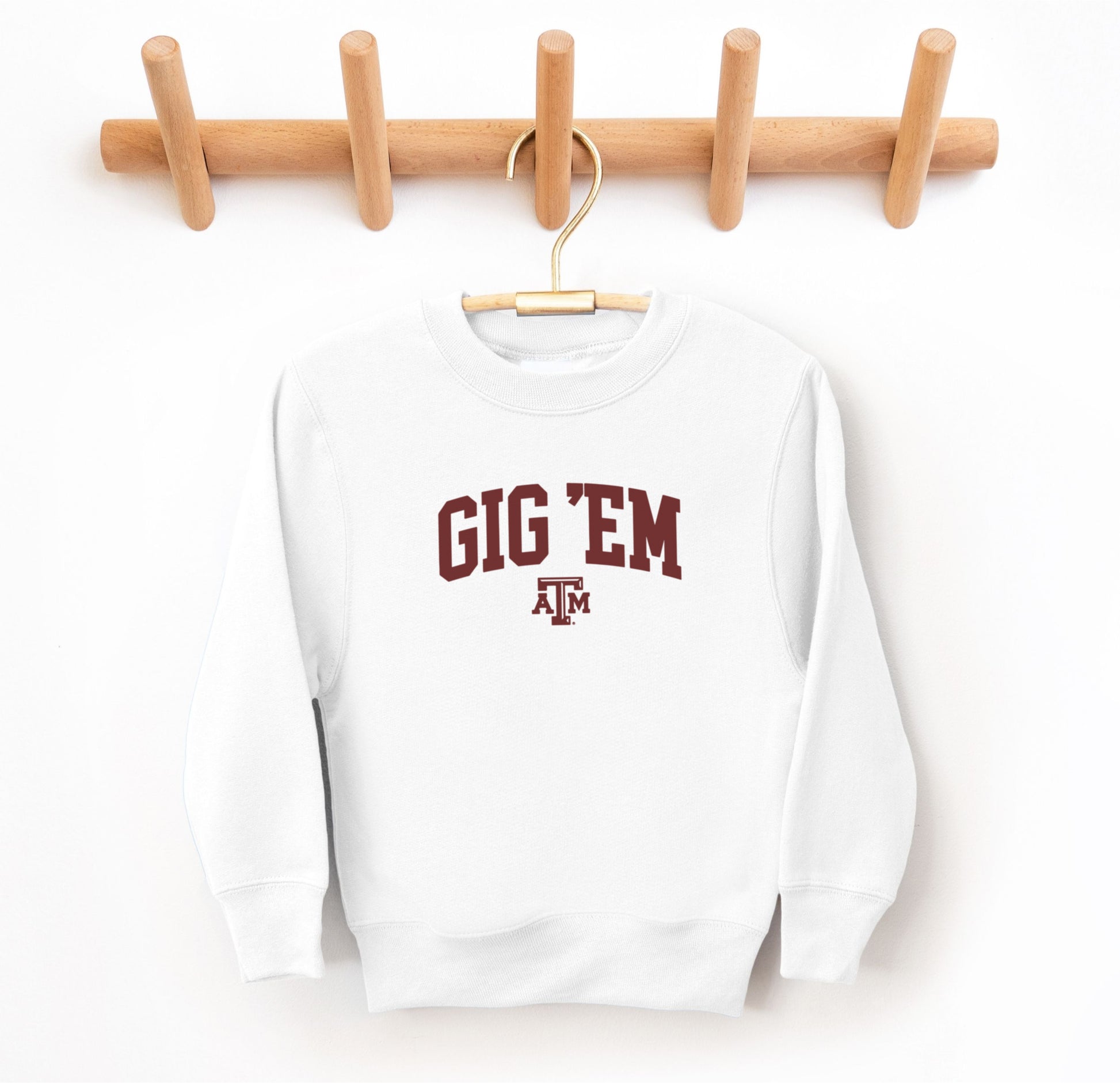 The White Youth Unisex Texas A&M Gig 'Em Collegiate Crewneck Sweatshirt lays flat on a white background. The ﻿Texas A&M Gig 'Em Collegiate﻿ graphic is in bold Maroon in a Collegiate style.