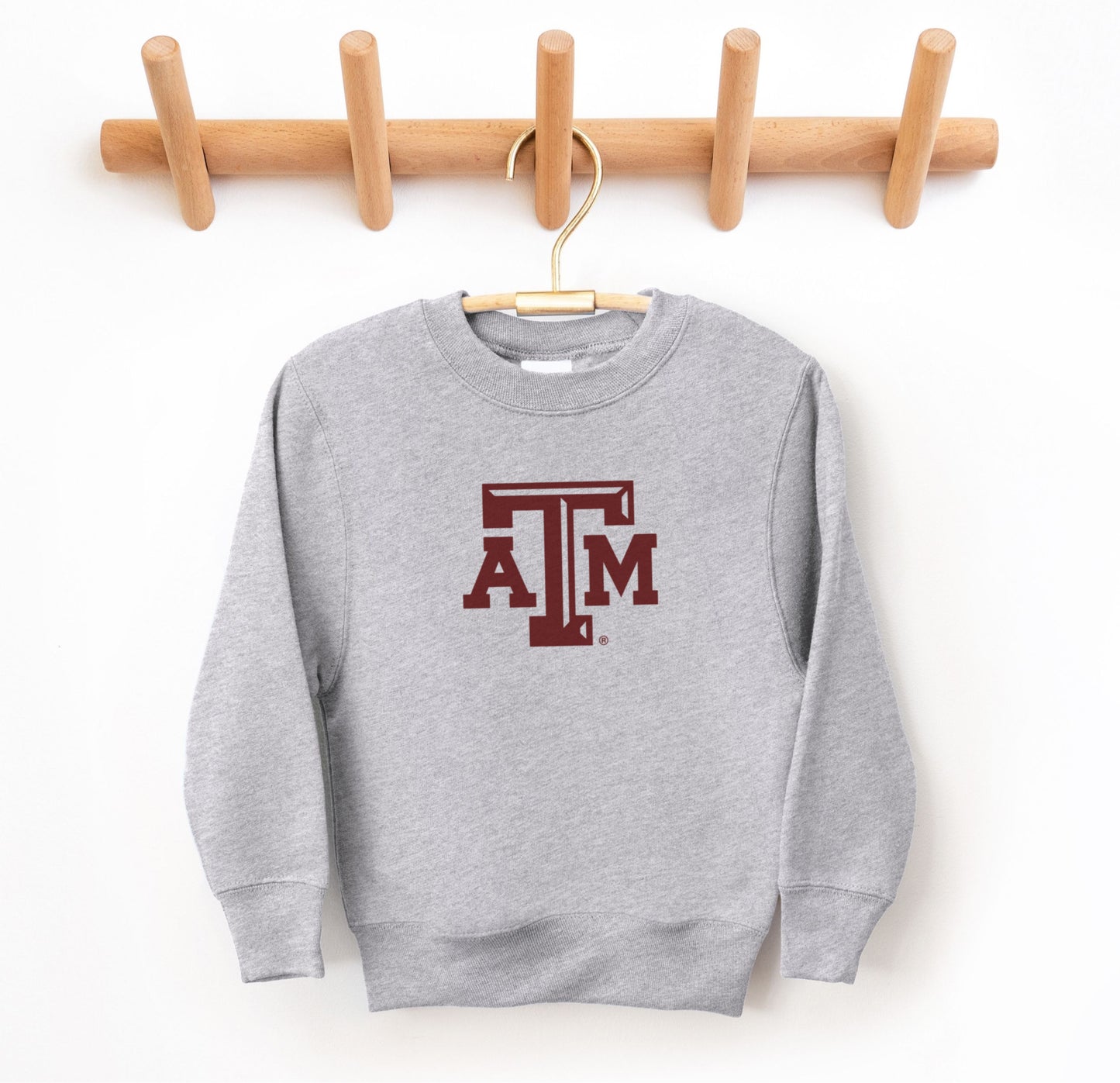 The Sport Grey Youth Unisex Texas A&M Logo Crewneck Sweatshirt lays flat on a white background. The ﻿Texas A&M Logo﻿ graphic is in bold Maroon in a Varsity style.