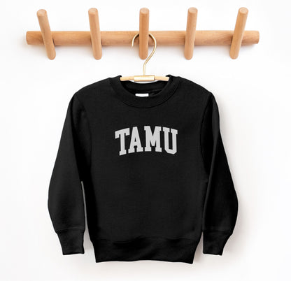 The Black Youth Unisex Texas A&M TAMU Crewneck Sweatshirt lays flat on a white background. The ﻿Texas A&M TAMU﻿ graphic is in bold White in a Collegiate style.