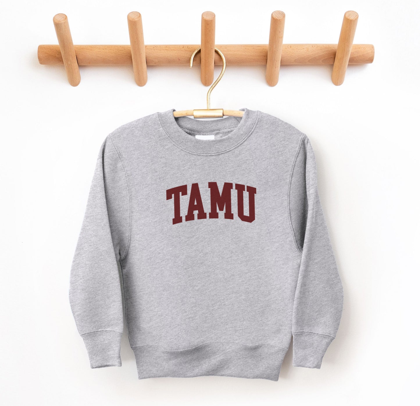 The Sport Grey Youth Unisex Texas A&M TAMU Crewneck Sweatshirt lays flat on a white background. The ﻿Texas A&M TAMU﻿ graphic is in bold Maroon in a Collegiate style.