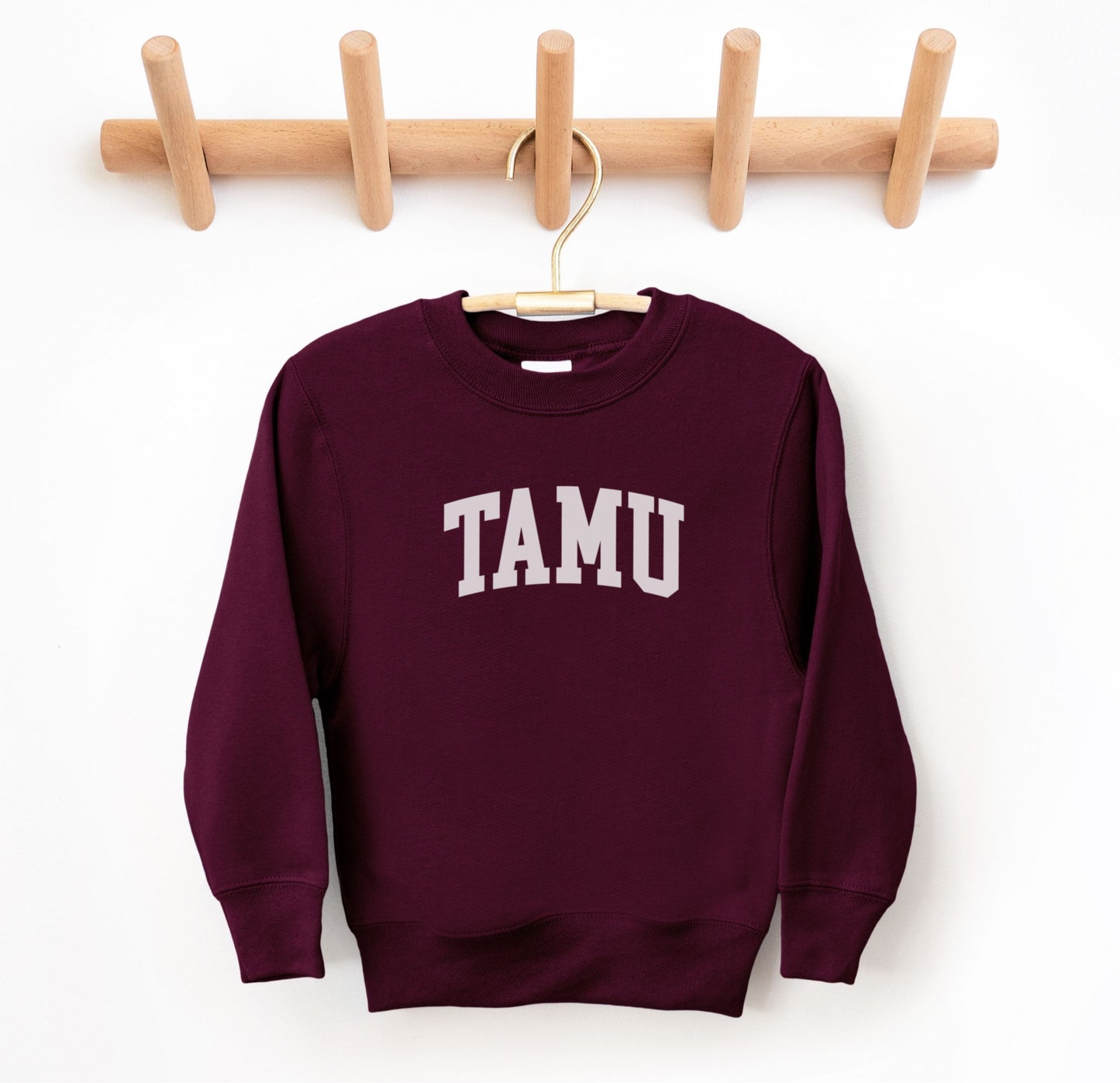 The Maroon Youth Unisex Texas A&M TAMU Crewneck Sweatshirt lays flat on a white background. The ﻿Texas A&M TAMU﻿ graphic is in bold White in a Collegiate style.