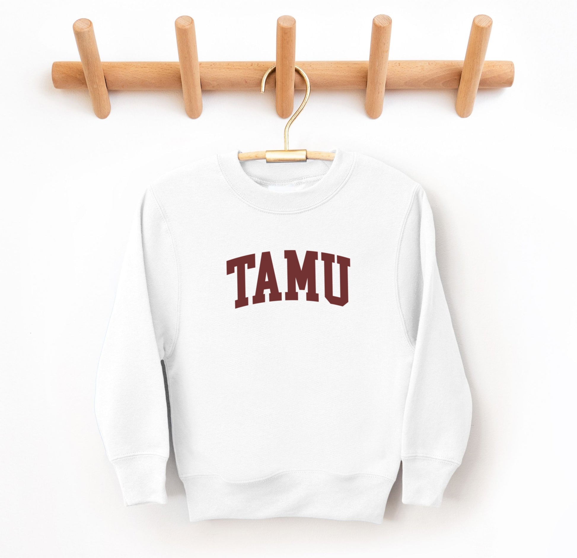 The White Youth Unisex Texas A&M TAMU Crewneck Sweatshirt lays flat on a white background. The ﻿Texas A&M TAMU﻿ graphic is in bold Maroon in a Collegiate style.