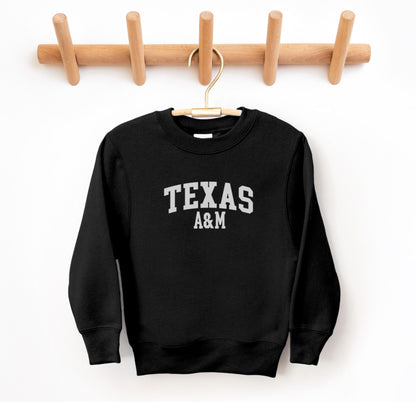 The Black Youth Unisex Texas A&M Varsity Crewneck Sweatshirt lays flat on a white background. The ﻿Texas A&M Varsity﻿ graphic is in bold White in a Collegiate style.