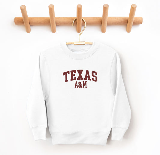 The White Youth Unisex Texas A&M Varsity Crewneck Sweatshirt lays flat on a white background. The ﻿Texas A&M Varsity﻿ graphic is in bold Maroon in a Collegiate style.