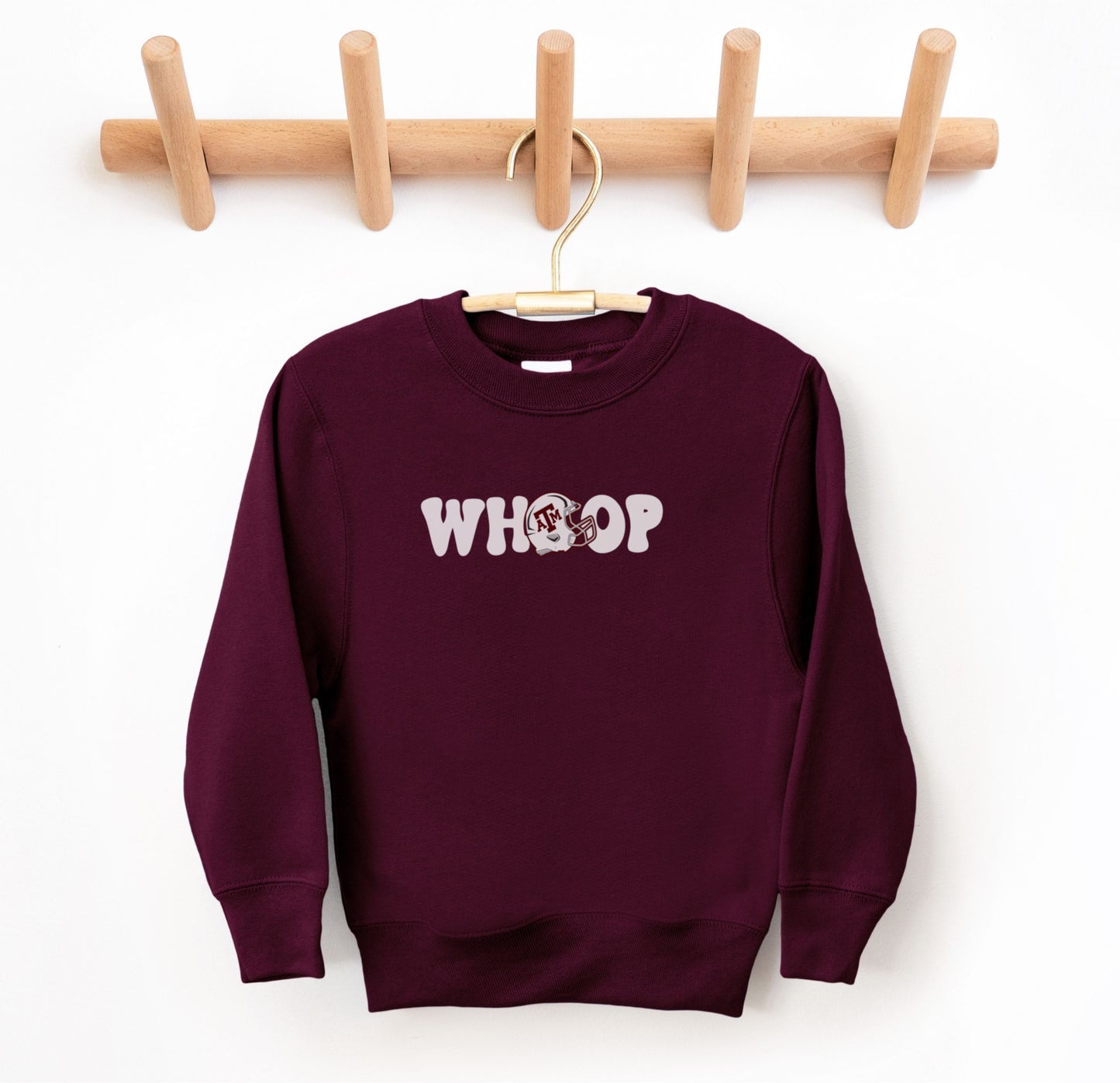 The Maroon Youth Unisex Texas A&M Retro Whoop Crewneck Sweatshirt lays flat on a white background. The ﻿Texas A&M Retro Whoop﻿ graphic is in bold White in a Vintage style.