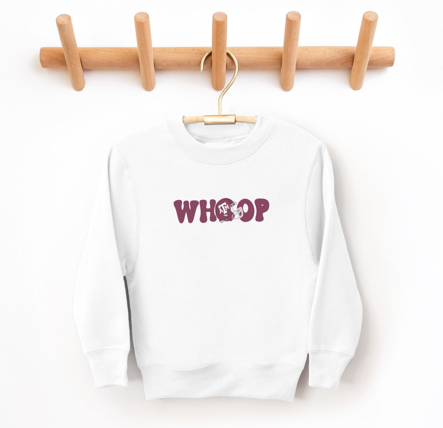 The White Youth Unisex Texas A&M Retro Whoop Crewneck Sweatshirt lays flat on a white background. The ﻿Texas A&M Retro Whoop﻿ graphic is in bold Maroon in a Vintage style.