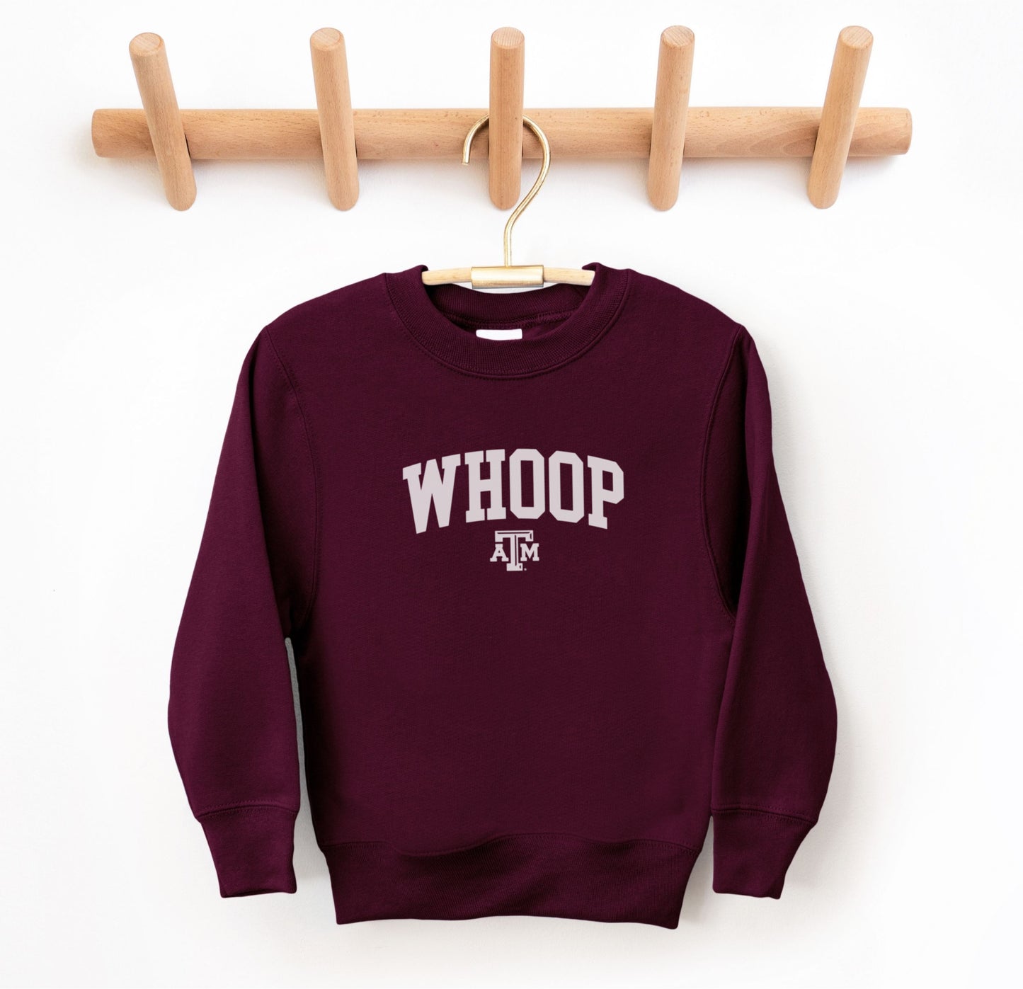 The Maroon Youth Unisex Texas A&M Whoop Collegiate Crewneck Sweatshirt lays flat on a white background. The ﻿Texas A&M Whoop Collegiate﻿ graphic is in bold White in a Varsity style.