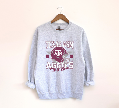 The Ash Grey Texas A&M Aggies Football Crewneck Sweatshirt lays flat on a white background. The ﻿Texas A&M Aggies Football﻿ graphic is in bold Unisex in a Varsity style.