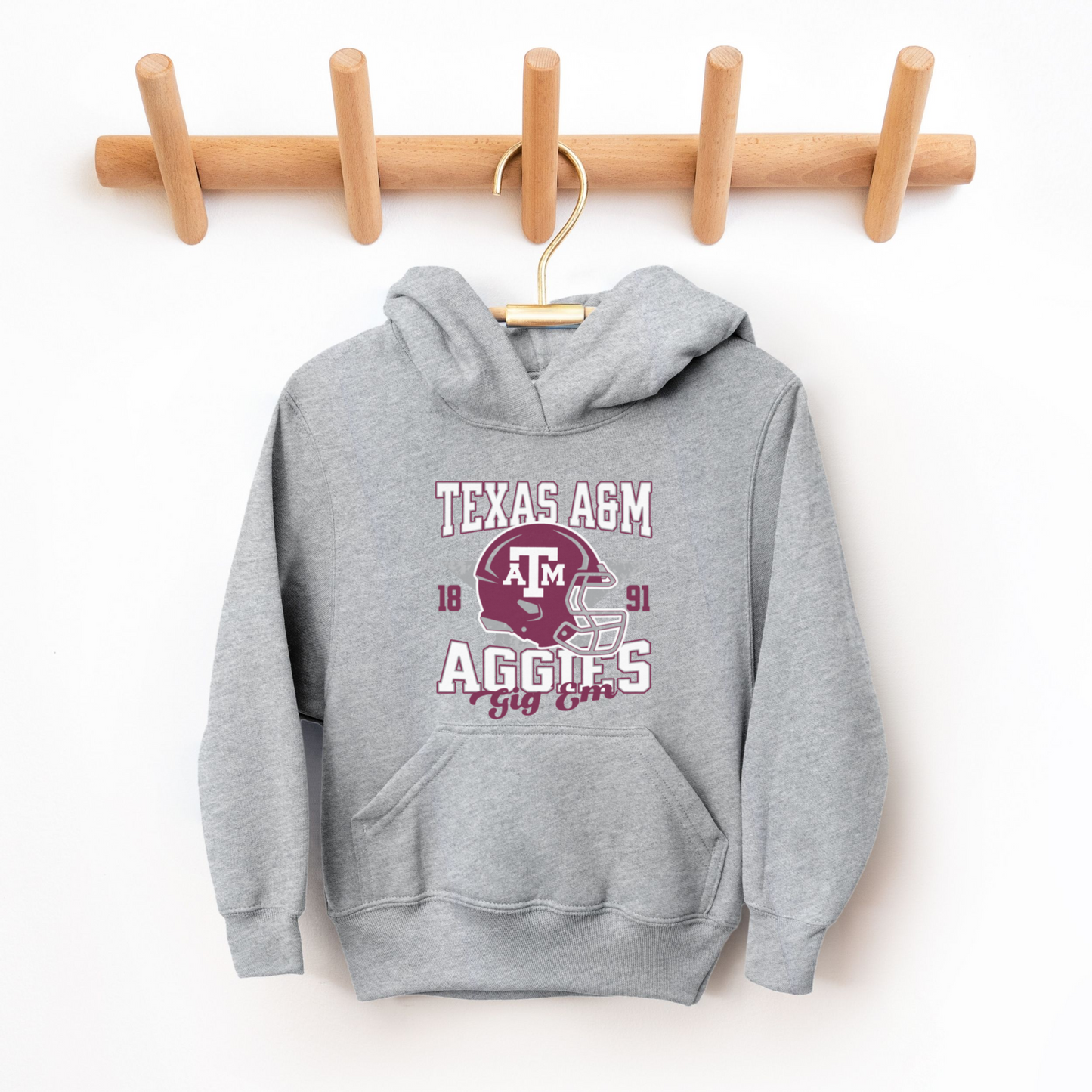 The Sport Grey Texas A&M Aggies Football Hooded Sweatshirt lays flat on a white background. The ﻿Texas A&M Aggies Football﻿ graphic is in bold Multicolor in a Varsity style.