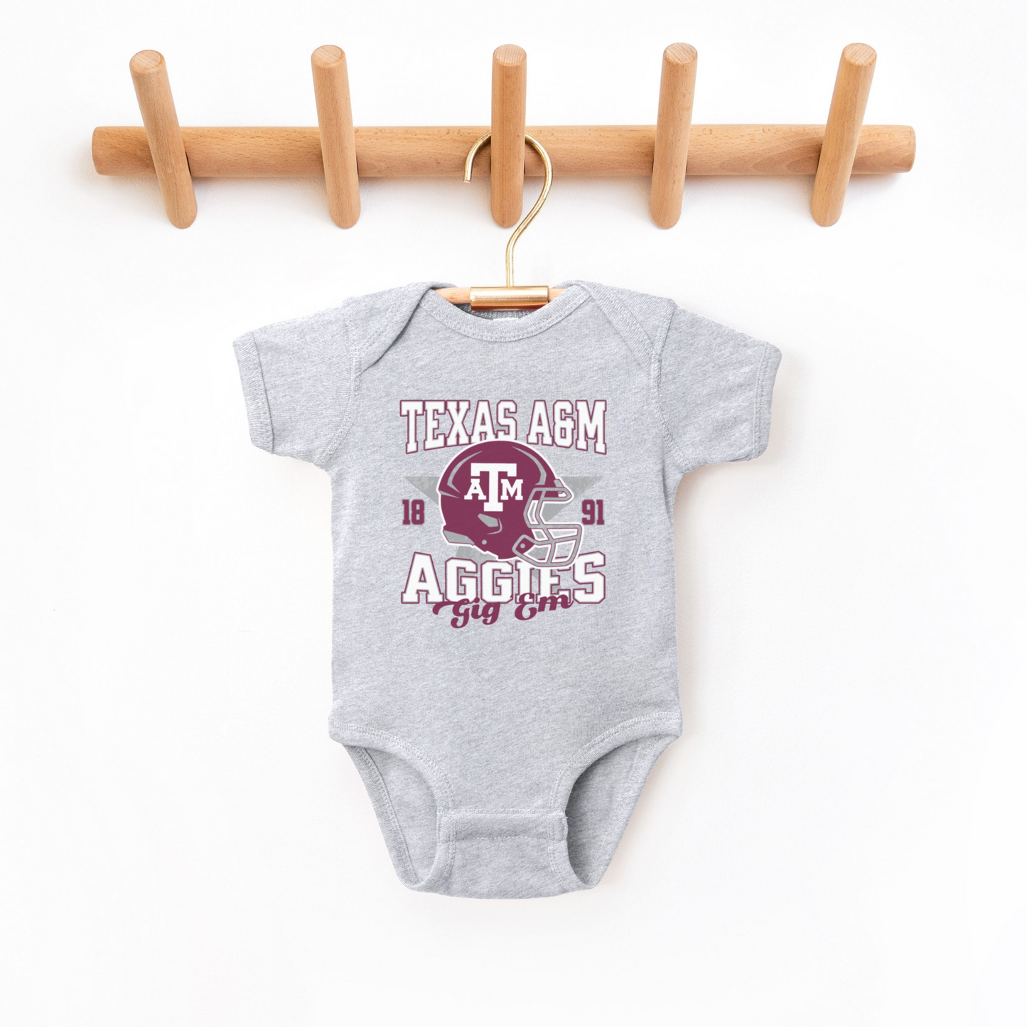 The Heather Grey Texas A&M Aggies Football Bodysuit lays flat on a white background. The ﻿Texas A&M Aggies Football﻿ graphic is in bold Multicolor in a Varsity style.