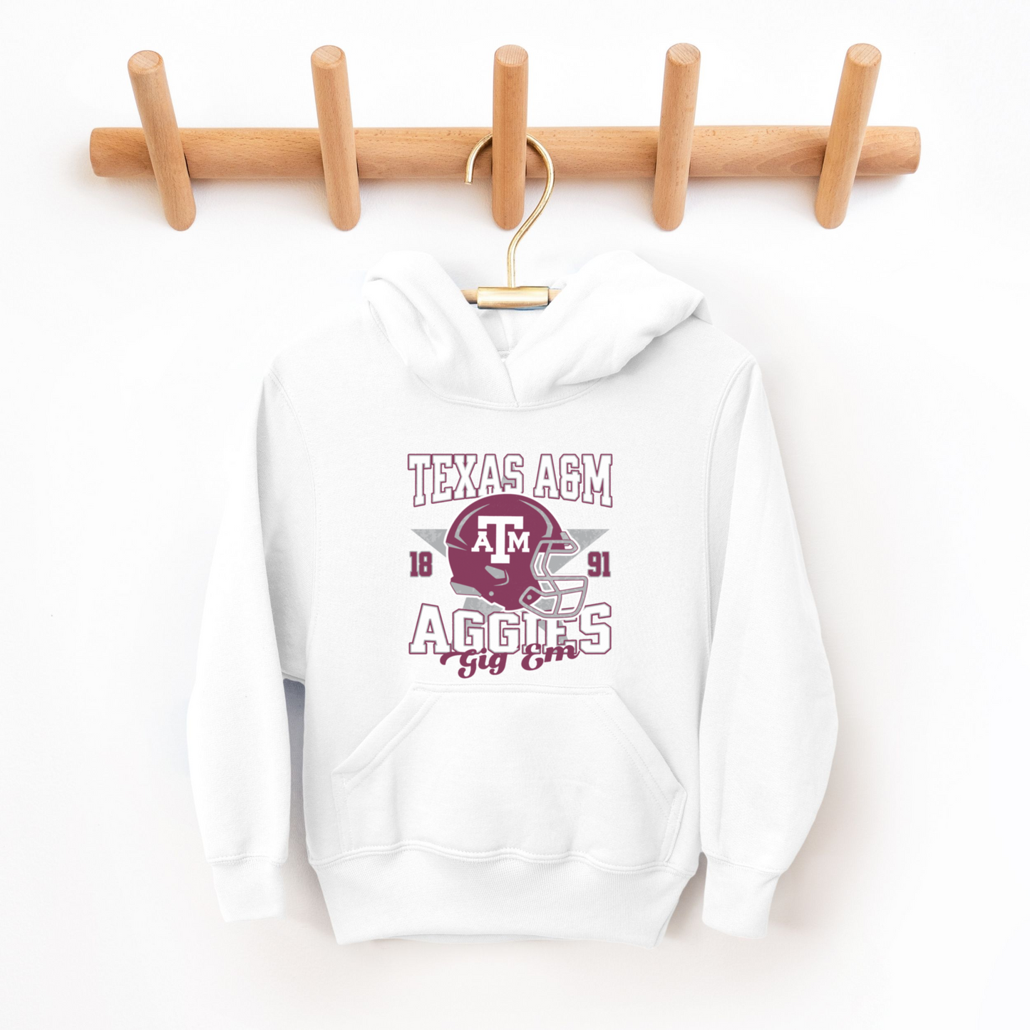 A model wears the White Texas A&M Aggies Football Hooded Sweatshirt.  The ﻿Texas A&M Aggies Football﻿ graphic is in bold Multicolor in a Varsity style.