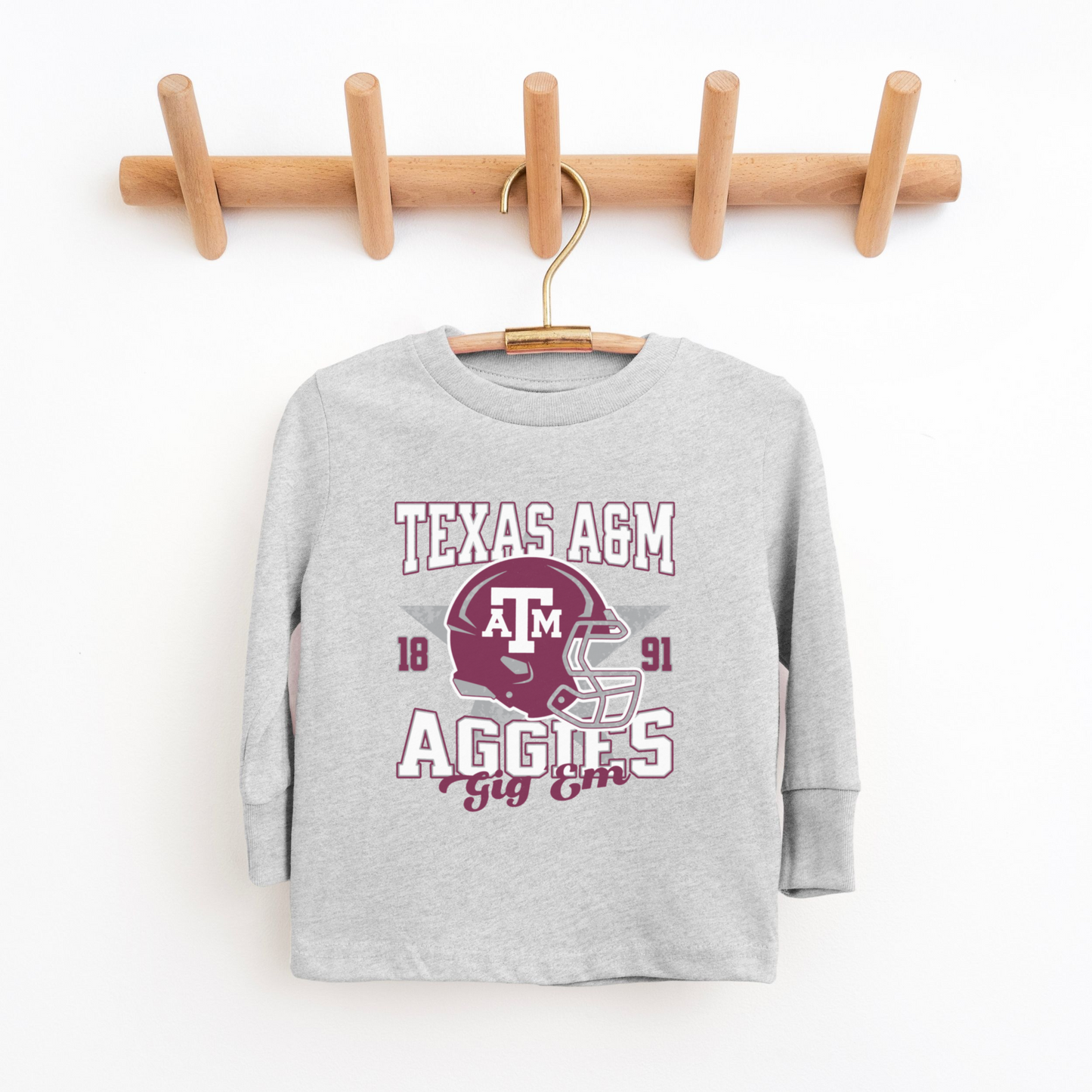 The Heather Grey Texas A&M Aggies Football Long Sleeve T-shirt lays flat on a white background. The ﻿Texas A&M Aggies Football﻿ graphic is in bold Multicolor in a Varsity style.