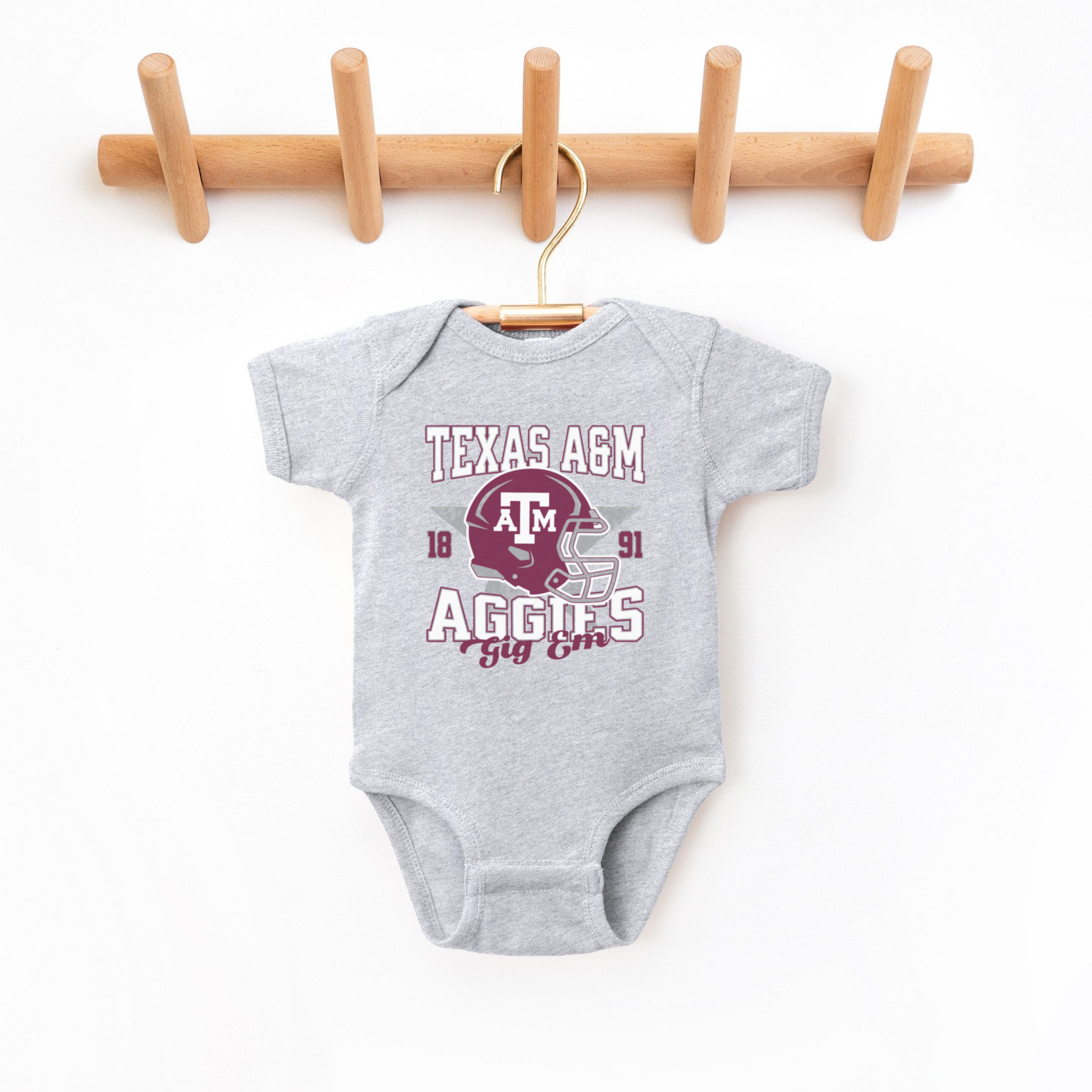 The Heather Grey Texas A&M Aggies Football Bodysuit lays flat on a white background. The ﻿Texas A&M Aggies Football﻿ graphic is in bold Multicolor in a Varsity style.